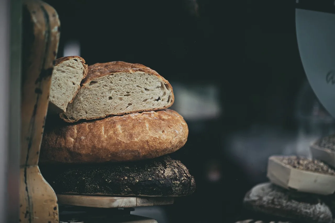 Angeschnittene Brotlaibe auf einem Holzregal vor dunklem Hintergrund